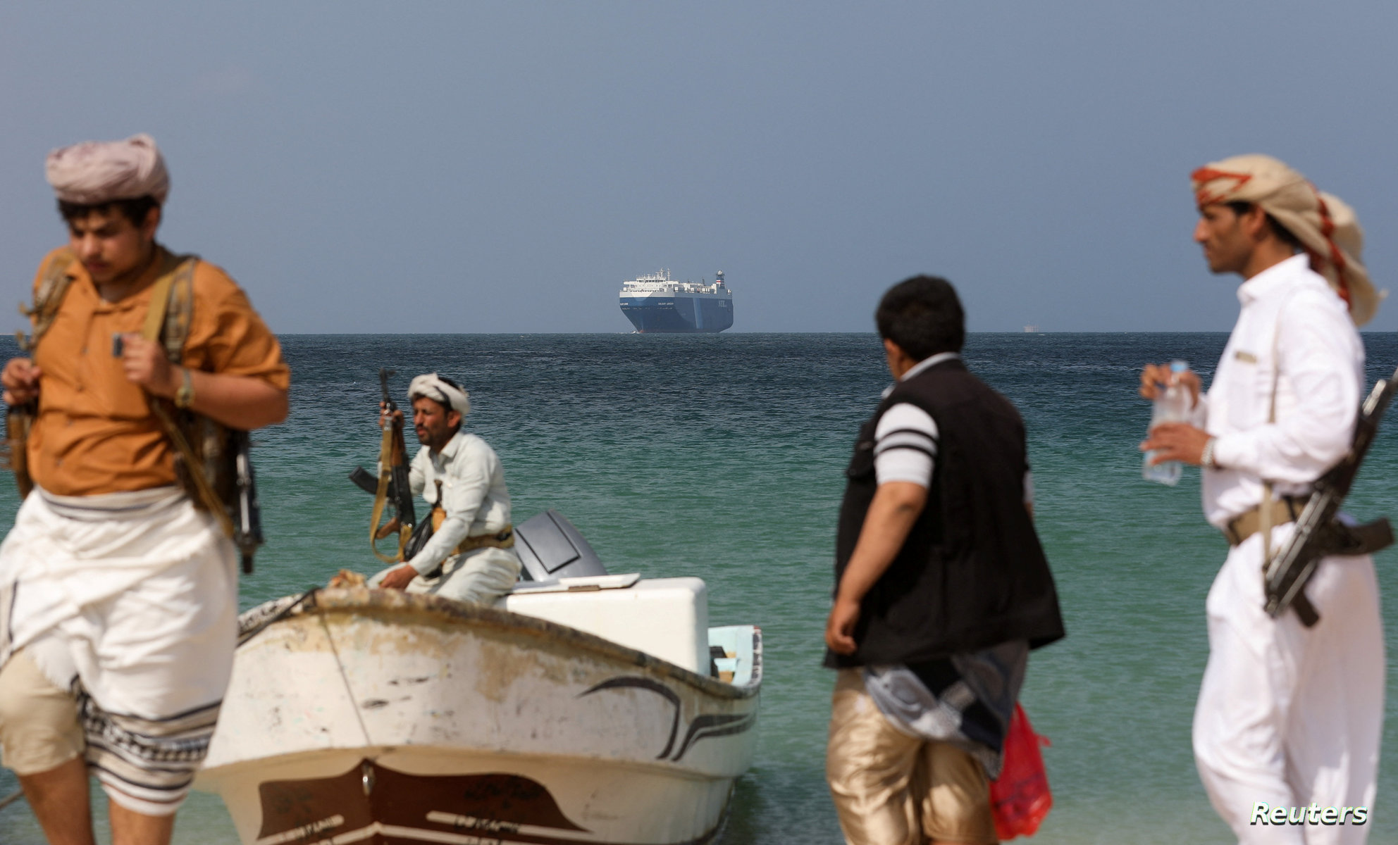 Armed men stand on the beach as the Galaxy Leader commercial ship, seized by Yemen’s Houthis last month, is anchored off the coast of al-Salif الحوثيون يهددون بتصعيد الهجمات ضد إسرائيل
