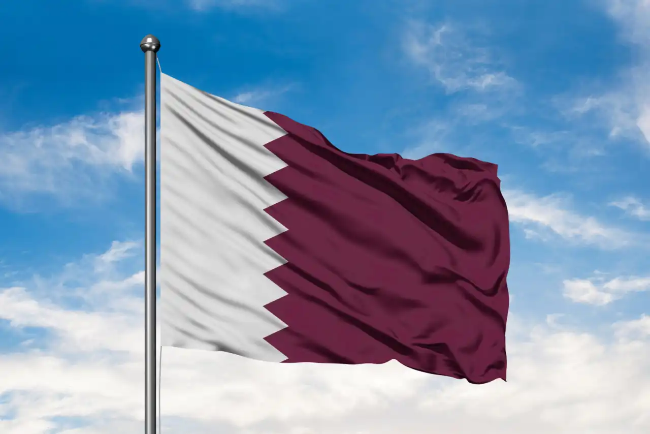 Flag of Qatar waving in the wind against white cloudy blue sky. Qatari flag.